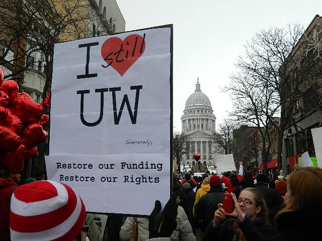 A student holding and "I still *heart* UW sign in front of the State Capitol.